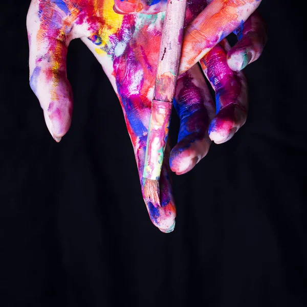 Siyah arka plan üzerine fırça ile parlak renkli boya sanatçının eller.