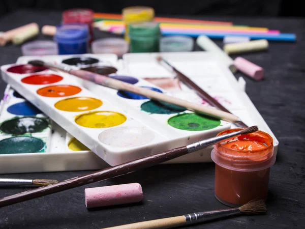 Pintura multicolor brillante, pasteles, lápices de colores, lápices de colores, pinceles sobre un fondo de madera negro. Listos para el artista. Educación . — Foto de Stock