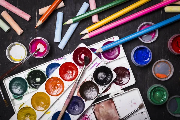 Pintura multicolor brillante, pasteles, lápices de colores, lápices de colores, pinceles sobre un fondo de madera negro. Listos para el artista. Educación . — Foto de Stock