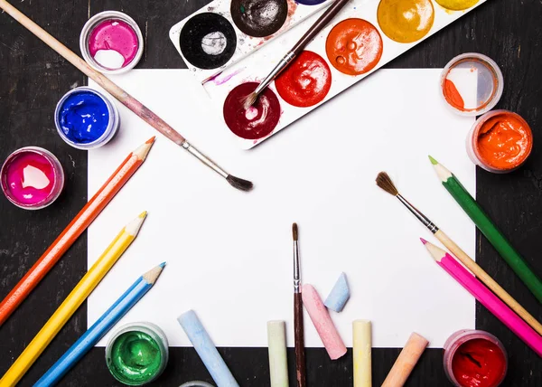Pintura multicolor brillante, pasteles, lápices de colores, lápices de colores, pinceles sobre lámina blanca y fondo de madera negro. Listos para el artista. Educación . — Foto de Stock