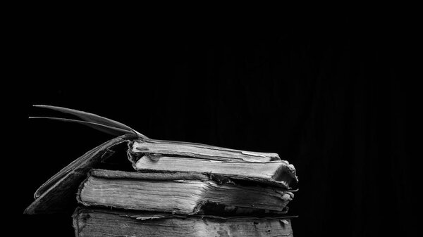 Old dilapidated wise books on dark background. Black and white photography
