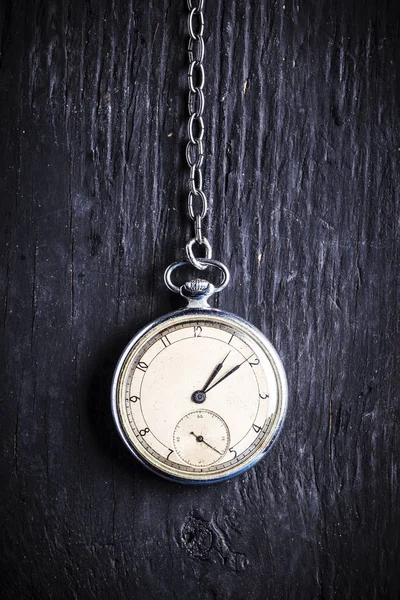 Antique clock on an old chain on a dark wooden background