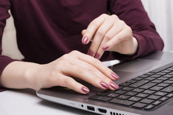 Female hand with a neat manicure typing text on laptop