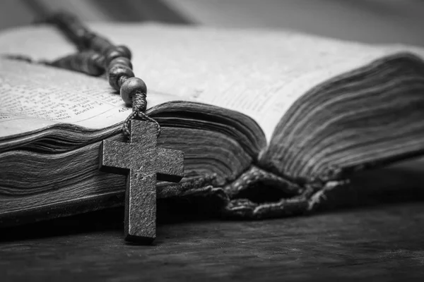 Rosario y cruz sobre la Biblia sobre un fondo de madera. Libro sagrado. Fotografía en blanco y negro . —  Fotos de Stock