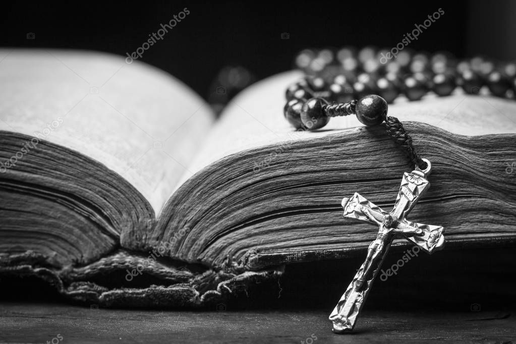 Rosary and cross on the Bible on a wooden background. Holy book. Black