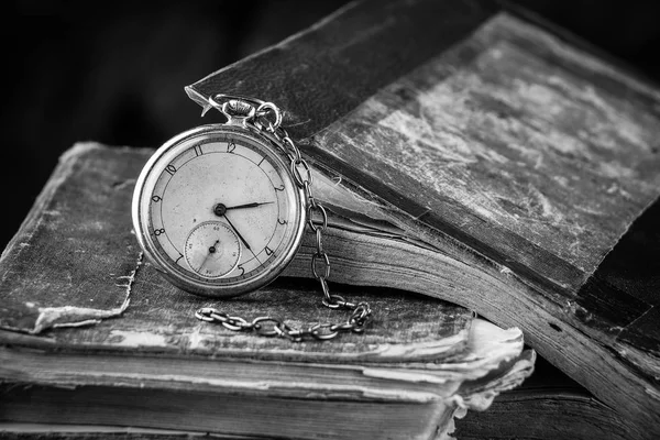 Reloj decadente en el fondo de viejos libros de mala calidad. Fotografía en blanco y negro Imagen De Stock