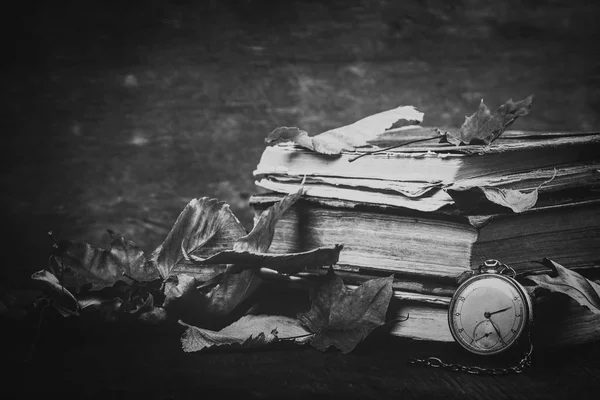 Fekete-fehér fényképezés. Pusztuló óra, a régi kopott bölcs könyvek az őszi száraz levelek a sötét fából készült háttér — Stock Fotó