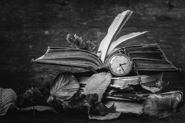 Zwart-wit fotografie. Vervallend klok op het oude shabby verstandig boeken met herfst droge bladeren op de donkere houten achtergrond — Stockfoto