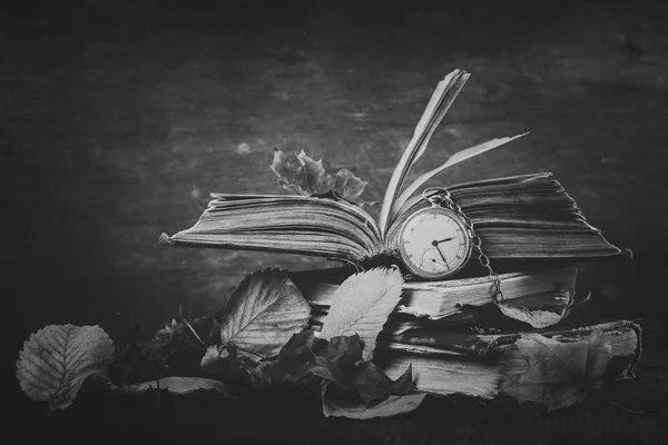 Pusztuló óra, a régi kopott bölcs könyvek az őszi száraz levelek a sötét fából készült háttér. Fekete-fehér fotózás — Stock Fotó