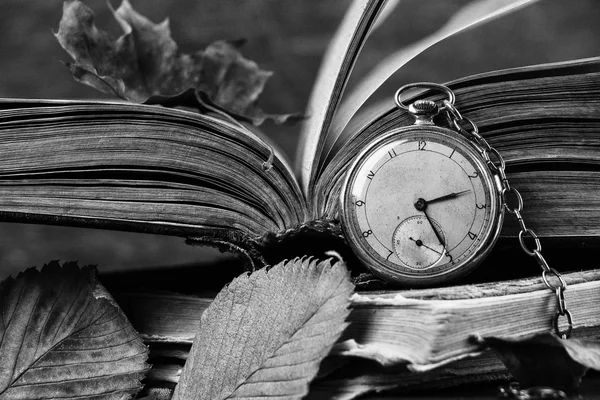 Reloj en decadencia en los viejos libros sabios de mala calidad con hojas secas de otoño sobre el fondo de madera oscura. Fotografía en blanco y negro — Foto de Stock