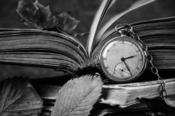 Reloj en decadencia en los viejos libros sabios de mala calidad con hojas secas de otoño sobre el fondo de madera oscura. Fotografía en blanco y negro — Foto de Stock