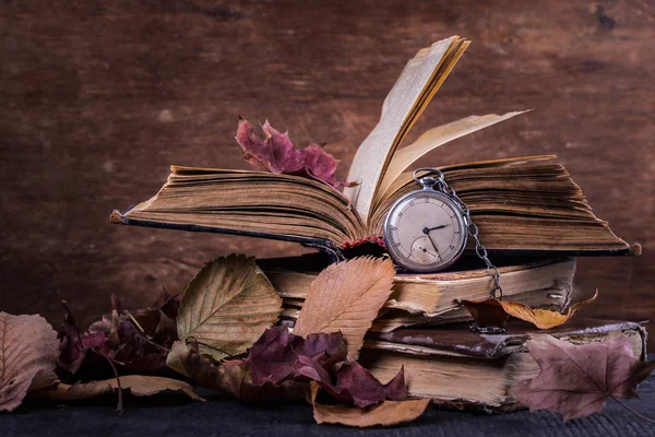 Reloj decadente en los viejos libros sabios de mala calidad con hojas amarillas secas de otoño sobre el fondo de madera oscura Imagen De Stock