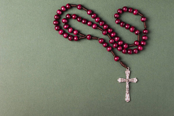 Pink Rosary on a green background with space for writing Christian cross.