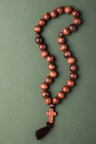 Wooden  rosary and cross on green background.