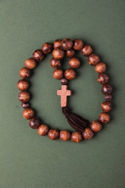 Wooden  rosary and cross on green background.