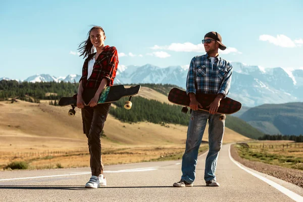Yolda kaykay yapan gençlerin portresi. Genç bir adam ve kadın, güneşli bir günde dağlarda uzun sörf yapıyorlar..