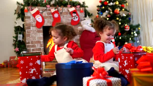 Zwei kleine Mädchen in Mützen von Weihnachtsmann auf dem Boden sitzend Witz — Stockvideo