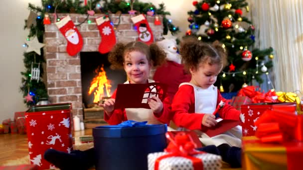 Zwei kleine Mädchen in Mützen von Weihnachtsmann auf dem Boden sitzend Witz — Stockvideo