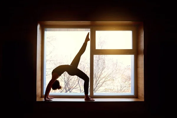 Woman doing yoga bridge on the background window. Exercising at — Stock Photo, Image