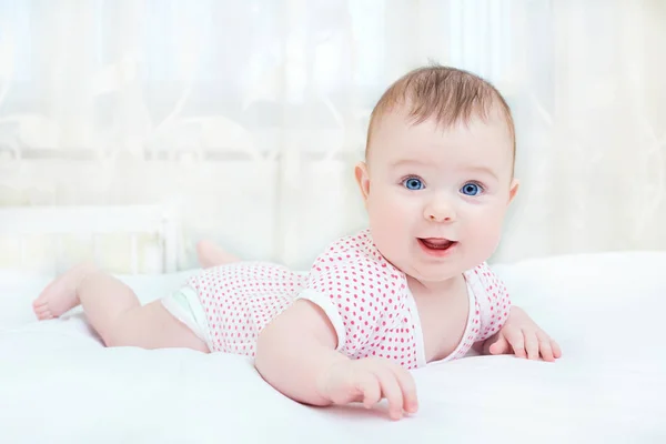 Bebê bonito sorrindo enquanto deitado em uma cama branca — Fotografia de Stock