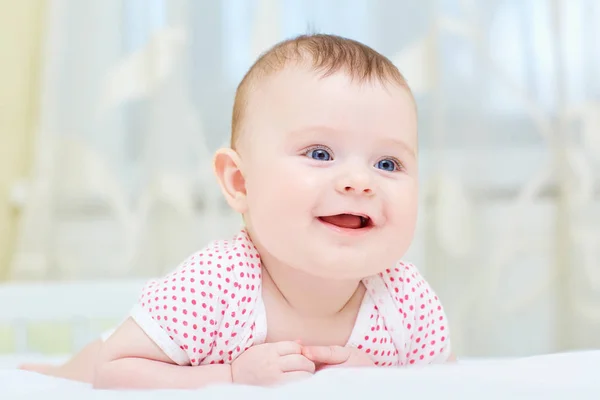 Baby, infant smiling while lying on a white bed — стоковое фото