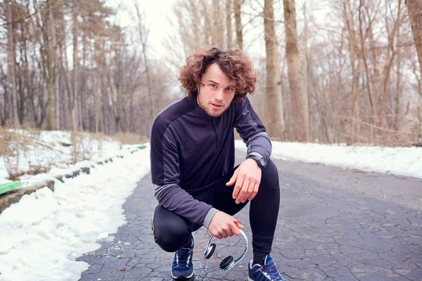 Joven hombre rizado con auriculares corriendo en un parque después — Foto de Stock