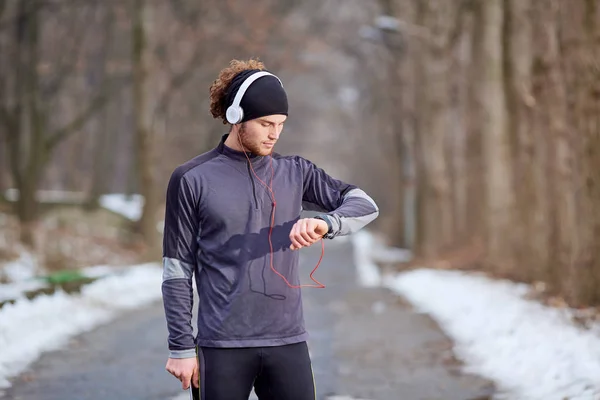 Man in sportswear jogging wearing headphones looking at his watc
