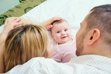 Annesi ve babası yatakta yatarken yanında gülümseyerek yürümeye başlayan çocuk