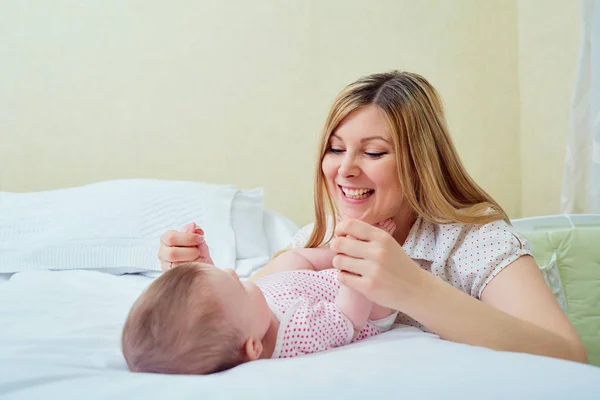 Anya játszik gyermekével az ágyon. Anya mosolyog a gyermekét — Stock Fotó