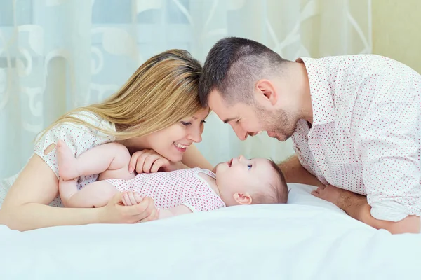 Madre y padre jugando con el bebé en la cama. Una familia feliz — Foto de Stock