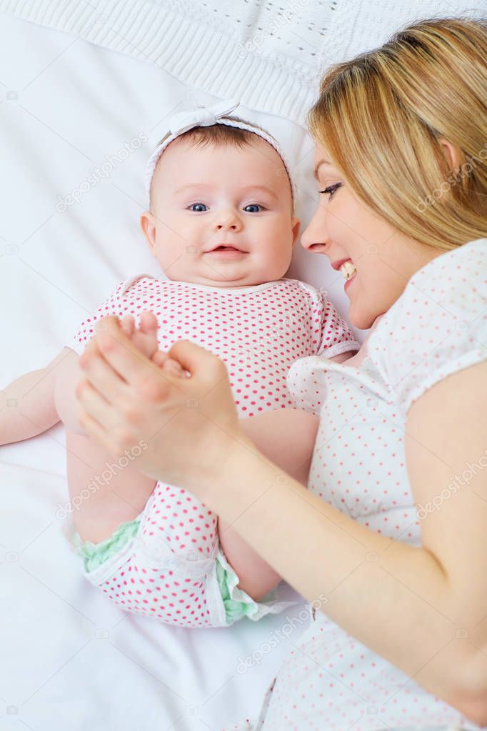 Mother playing with her baby on the bed. Mom smiles to her child