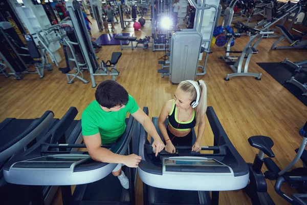 Personal trainer man with athletic girl on a treadmill in the gy