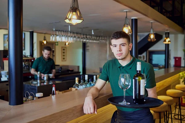 Ein Kellner hält ein Tablett mit einer Flasche Wein und Gläsern in der Bar — Stockfoto