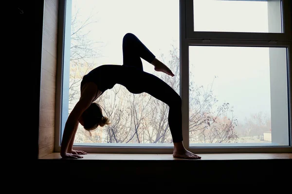 Woman doing yoga bridge on the background window. Exercising at — Stock Photo, Image