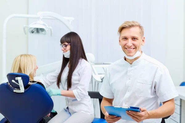 Le dentiste avec des documents dans ses mains sourit cabinet dentaire — Photo