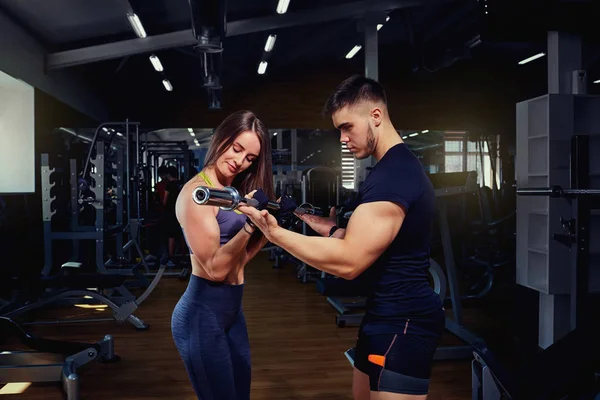Entrenador personal ayuda a una chica levantando pesas en el gimnasio — Foto de Stock