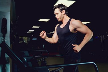 Adam atlet koyu spor salonunda bir koşu bandı üzerinde koşu çalışır