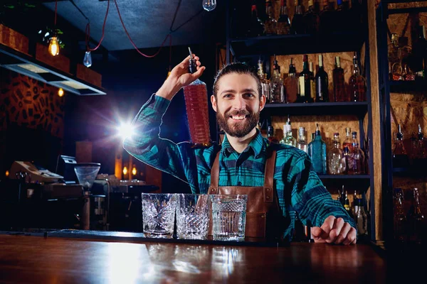 Un barman con una botella de alcohol sonríe riéndose del bar —  Fotos de Stock