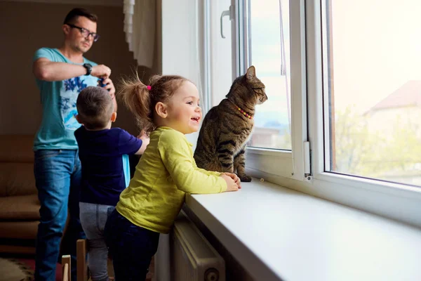 Šťastná rodina. Malá holčička se dívá z okna na pozadí — Stock fotografie