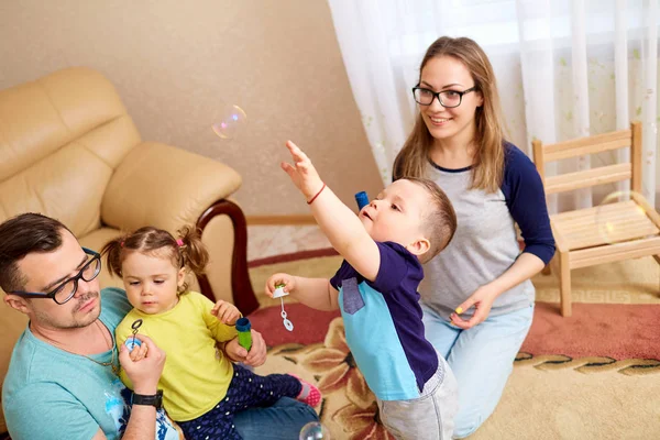 A família está brincando com bolhas de sabão no quarto — Fotografia de Stock