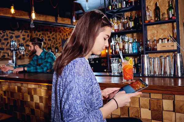 Ein Mädchen mit Cocktail lächelt mit Tablette hinter der Theke am b — Stockfoto