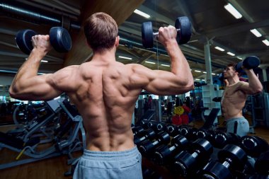 Spor salonunda onun kollarında dumbbells ile sportif bir adam arkadan görünüş