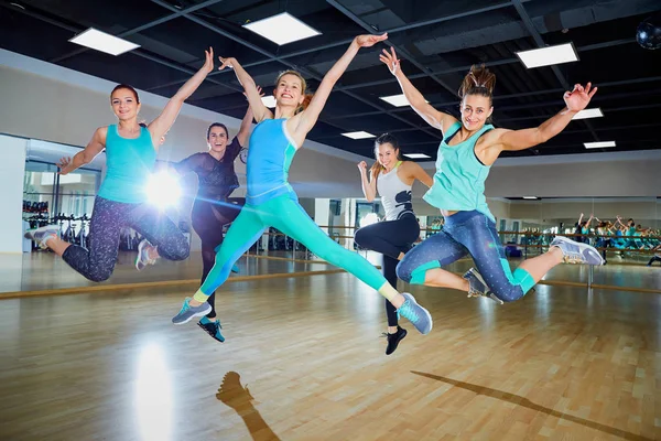 A group of girls jump with smiles in the gym