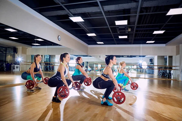 Entrenamiento en grupo. Las chicas hacen sentadillas con un bar en el gimnasio —  Fotos de Stock