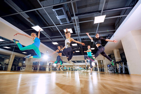 A group of girls jump with smiles in the gym