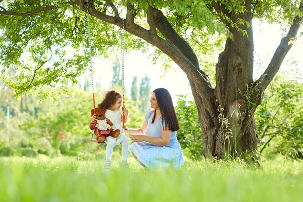 Mama toczy się na huśtawce childs, w parku, w lecie. — Zdjęcie stockowe