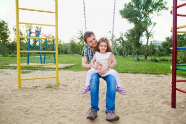 Baba ile çocuk oyun alanı, bir salıncak üzerinde