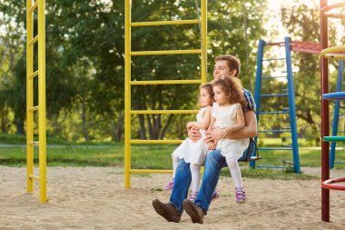 Baba ile çocuklar parkta salıncakta oynarken