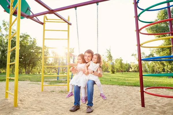 Baba ile çocuklar parkta salıncakta oynarken
