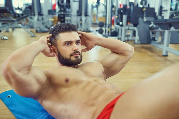 Culturista con barba hace ejercicios abdominales en el suelo en la g — Foto de Stock